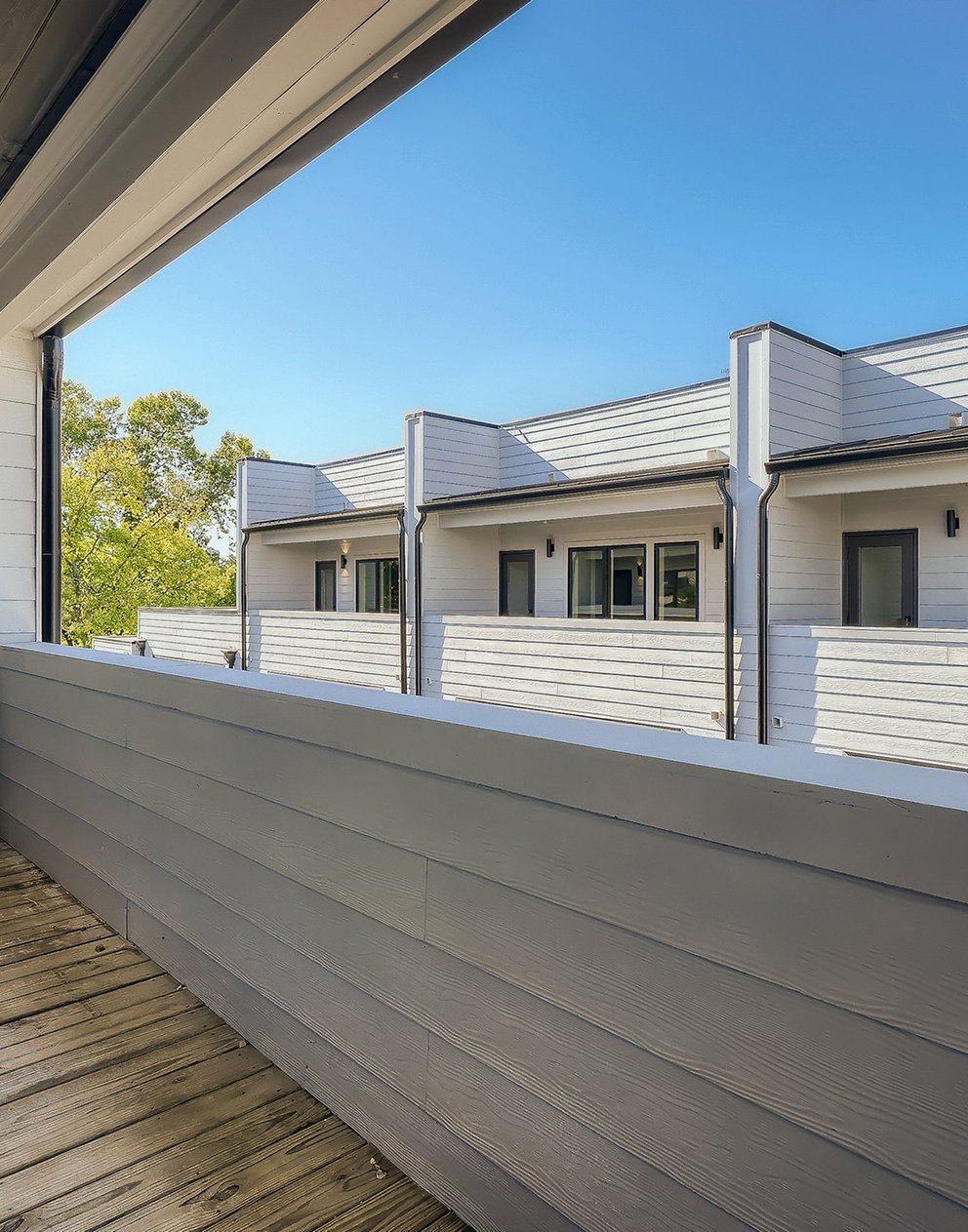 Finished modern multi-unit townhome exterior with white siding, seen from a covered deck